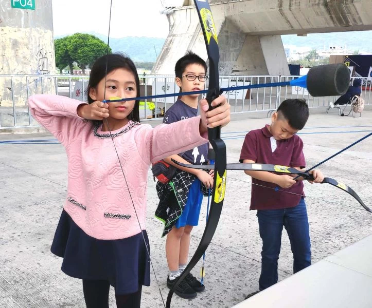 聽障奧運自由車國手莊詠智的女兒莊晴晴(前)體驗射箭架式十足。企業射箭聯盟/提供。
