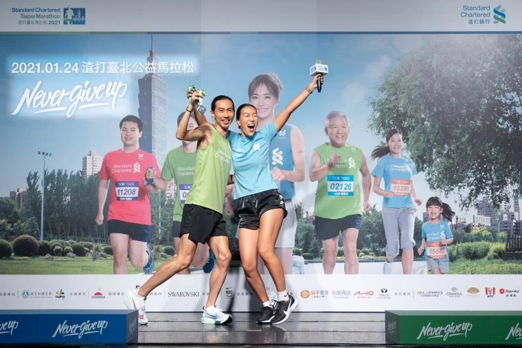 2021渣打臺北公益馬拉松超級戰隊隊長張嘉哲與時尚戰隊隊長莫莉,拿著施華洛世奇獎牌,現場示範完賽時尚照。大會提供