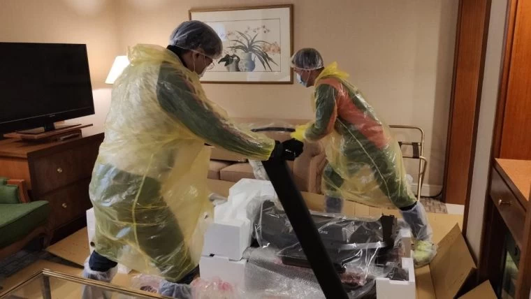 身著全套防護裝備的技師們在隔離客房內安裝跑步機。大會提供