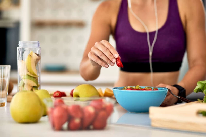 closeup athletic woman adding strawberries while making fruit salad kitchen