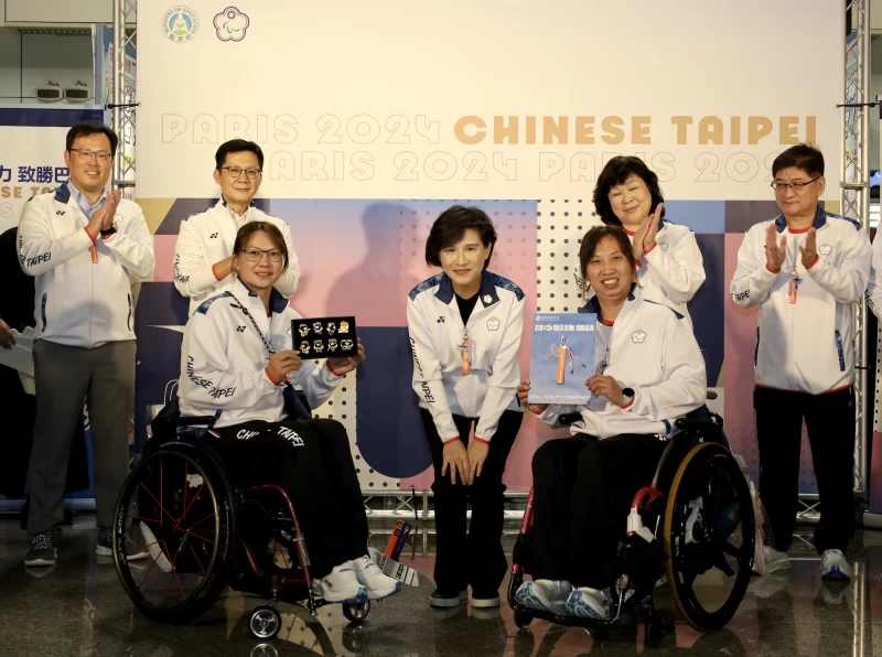 行政院鄭麗君副院長(中)贈送臺灣藍鵲吊飾及帕拉黑熊徽章予代表團成員，由羽球選手楊伊宸(左)及胡光秋代表受贈。體育署提供